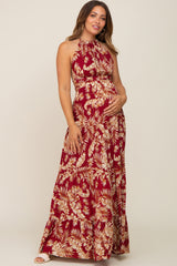 woman wearing a burgundy floral halter neck maternity maxi dress and cradling her baby bump