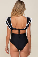 woman wearing a black maternity swimsuit with white trim and flutter sleeves, featuring a cutout back and tie detail