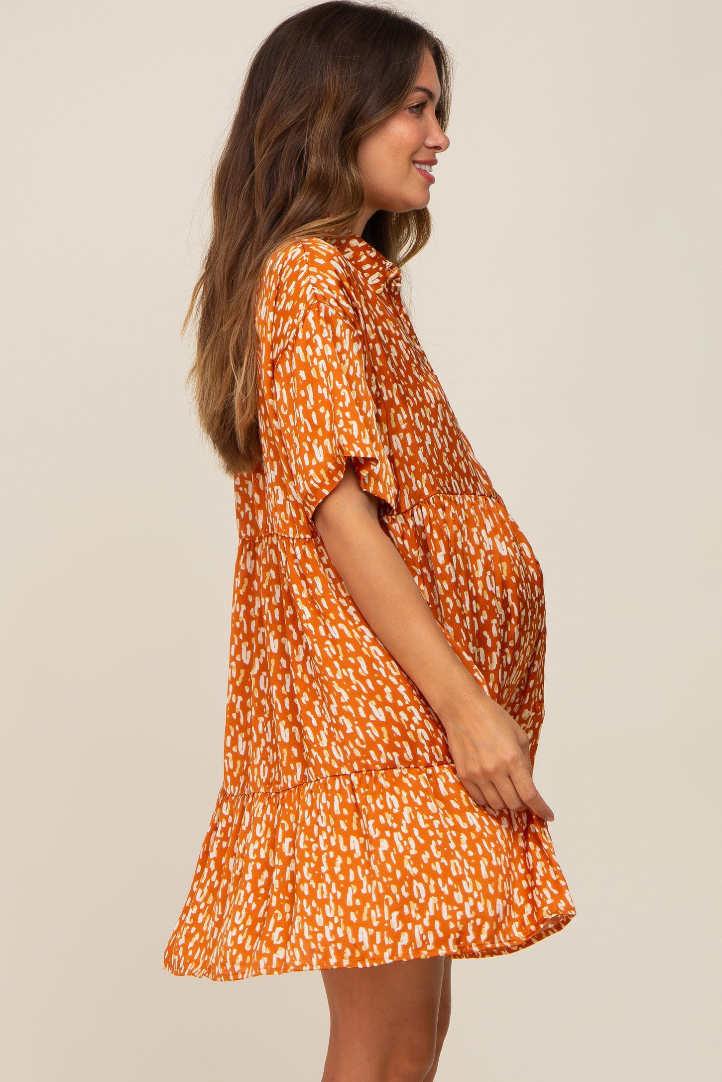 woman wearing an orange printed maternity dress with short sleeves and a flowy hem, showcasing her baby bump