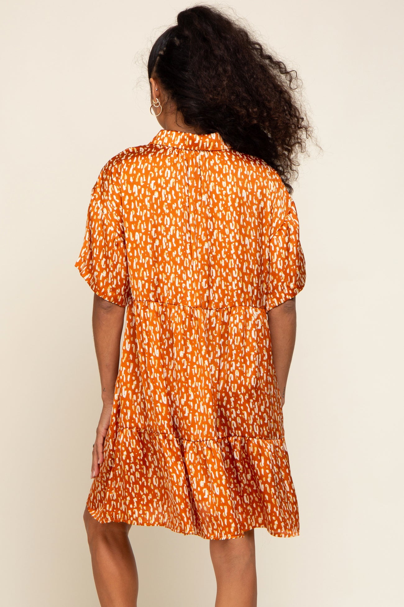 woman wearing an orange short sleeve mini dress with a playful print and tiered skirt, viewed from the back