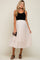 woman wearing a black ribbed maternity tank top and a light pink tulle midi skirt, holding a clutch bag