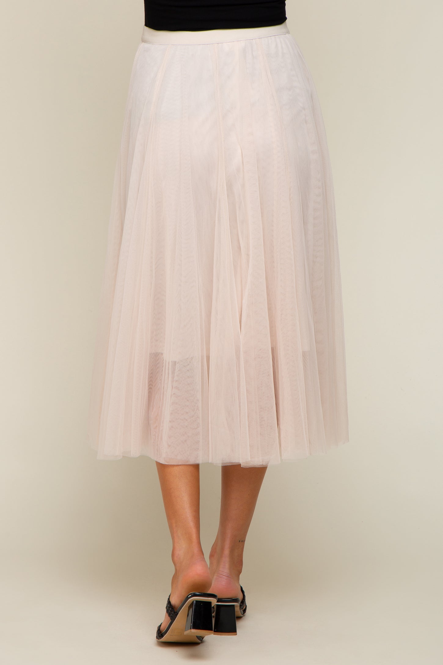 woman wearing a long pink tulle maternity skirt, view of the back, styled with a black top and heels