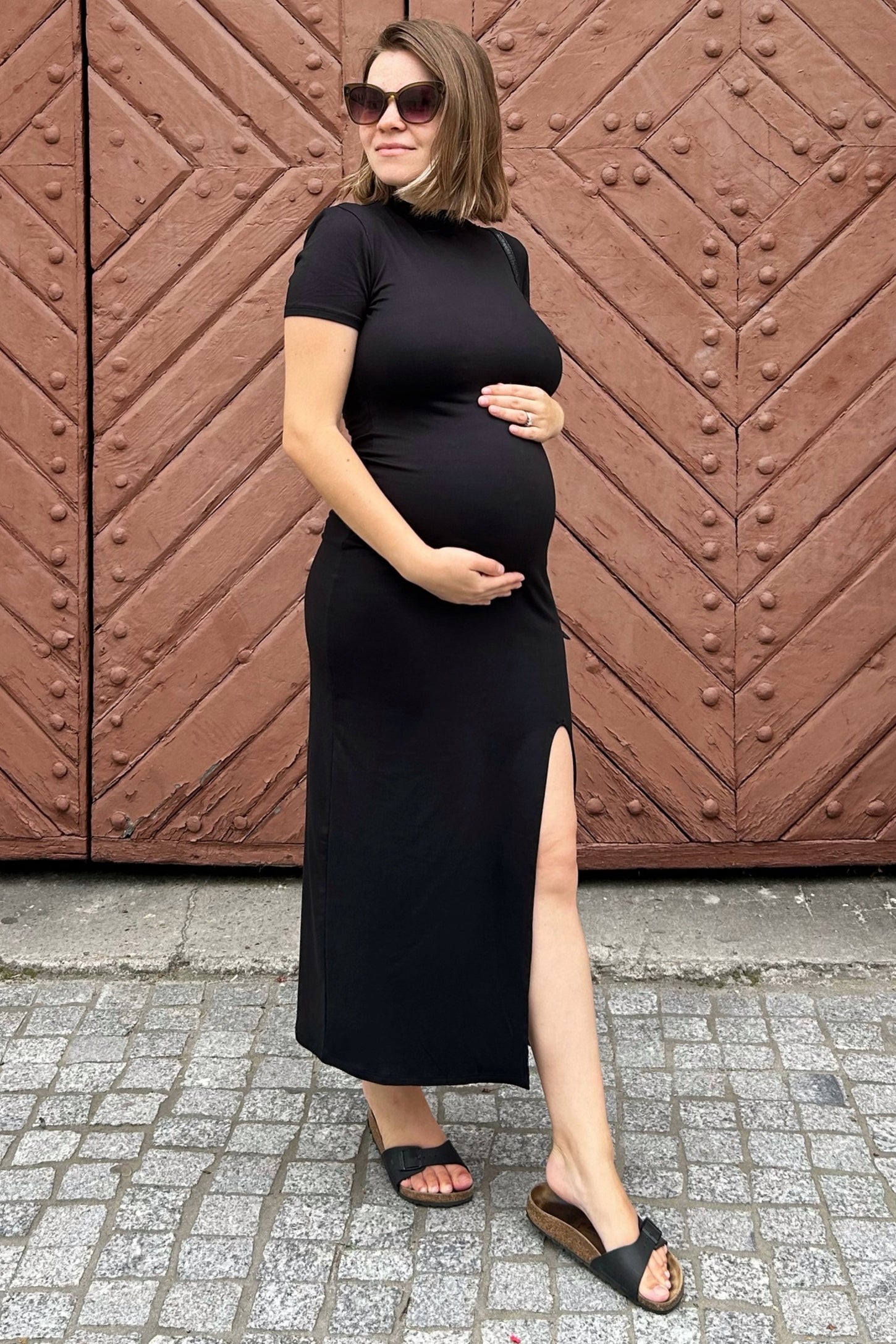 woman wearing a black short sleeve maternity dress with a side slit and a visible baby bump