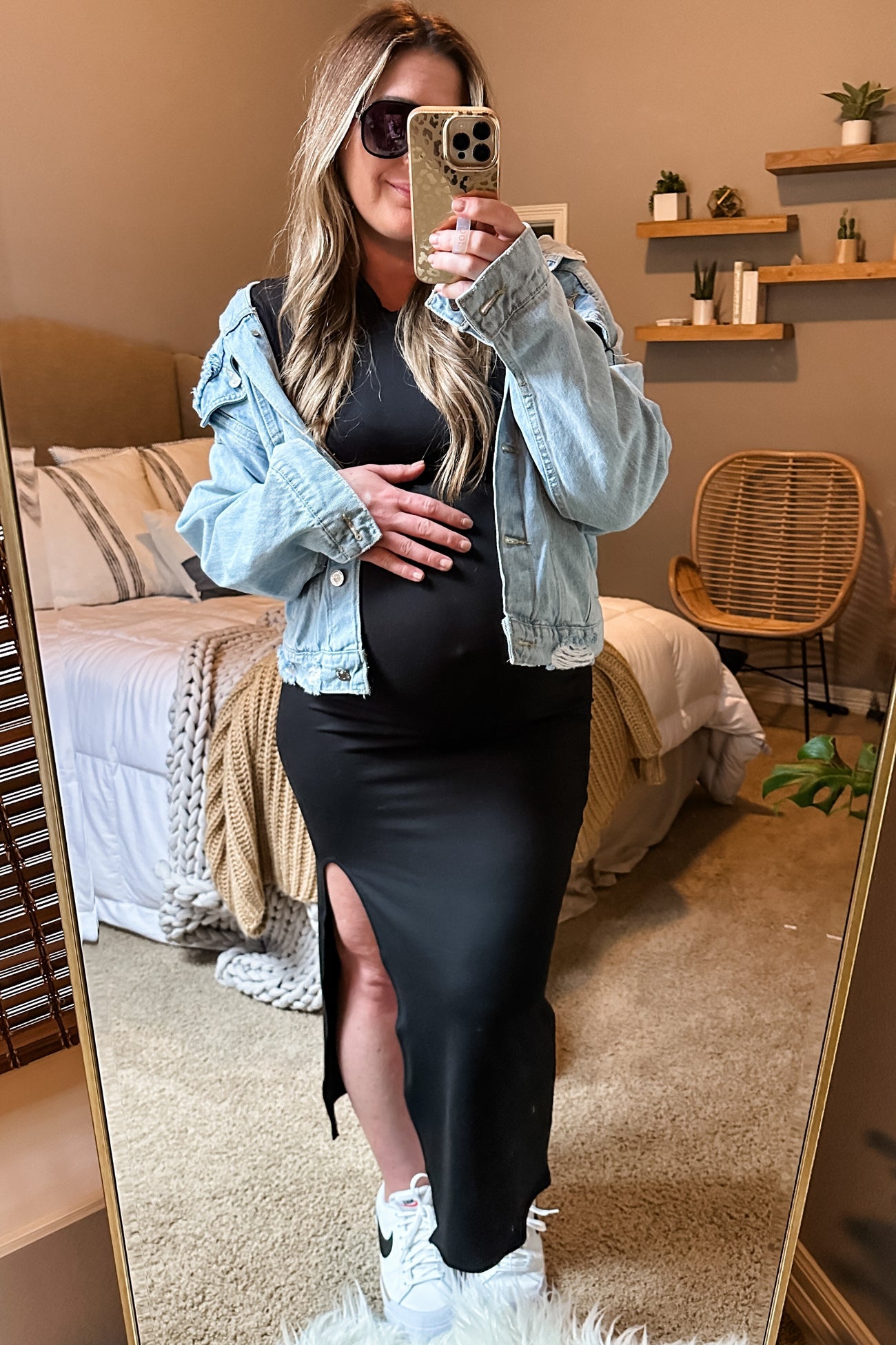 woman wearing a black maternity dress with a thigh-high slit and a denim jacket, holding her baby bump in a stylish setting