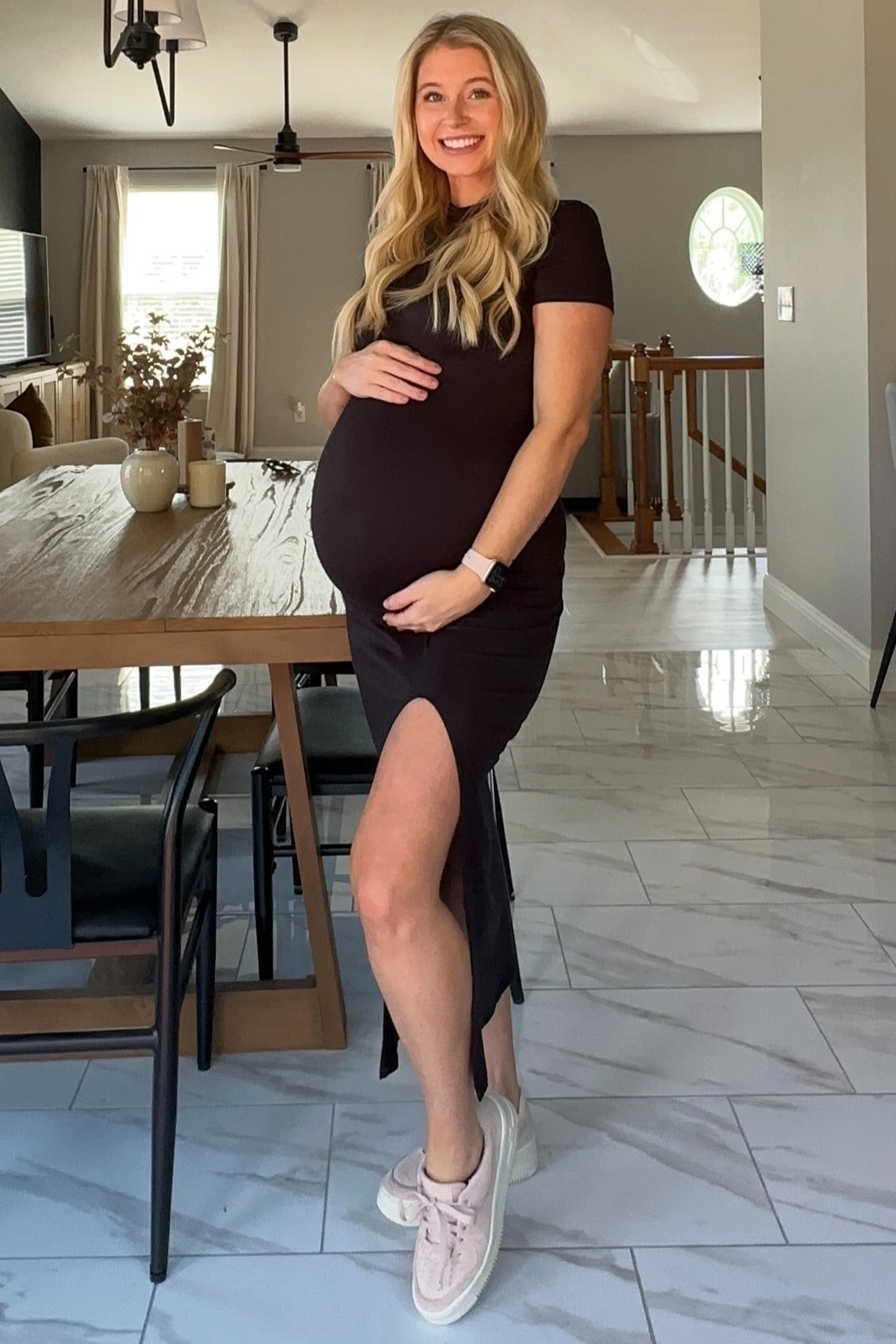 woman wearing a black maternity dress with a side slit and showing her baby bump, standing in a modern kitchen