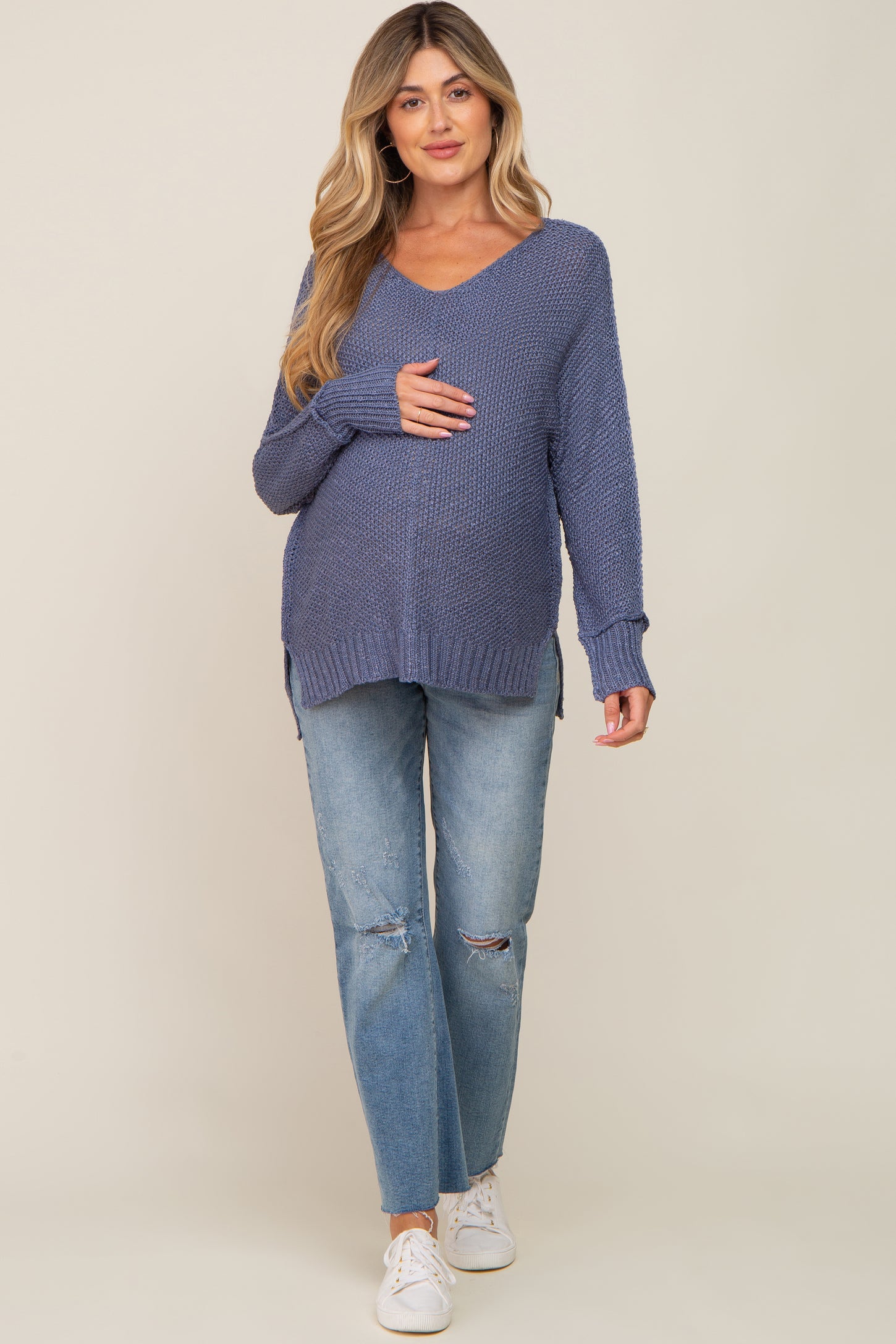 woman wearing a dark blue maternity sweater with a v-neck and holding her baby bump, paired with light blue distressed jeans