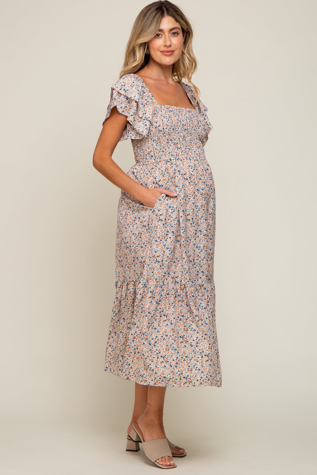 woman wearing a floral print maternity dress with ruffle sleeves and pockets, showcasing her baby bump