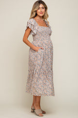 woman wearing a floral print maternity dress with ruffle sleeves and pockets, showcasing her baby bump