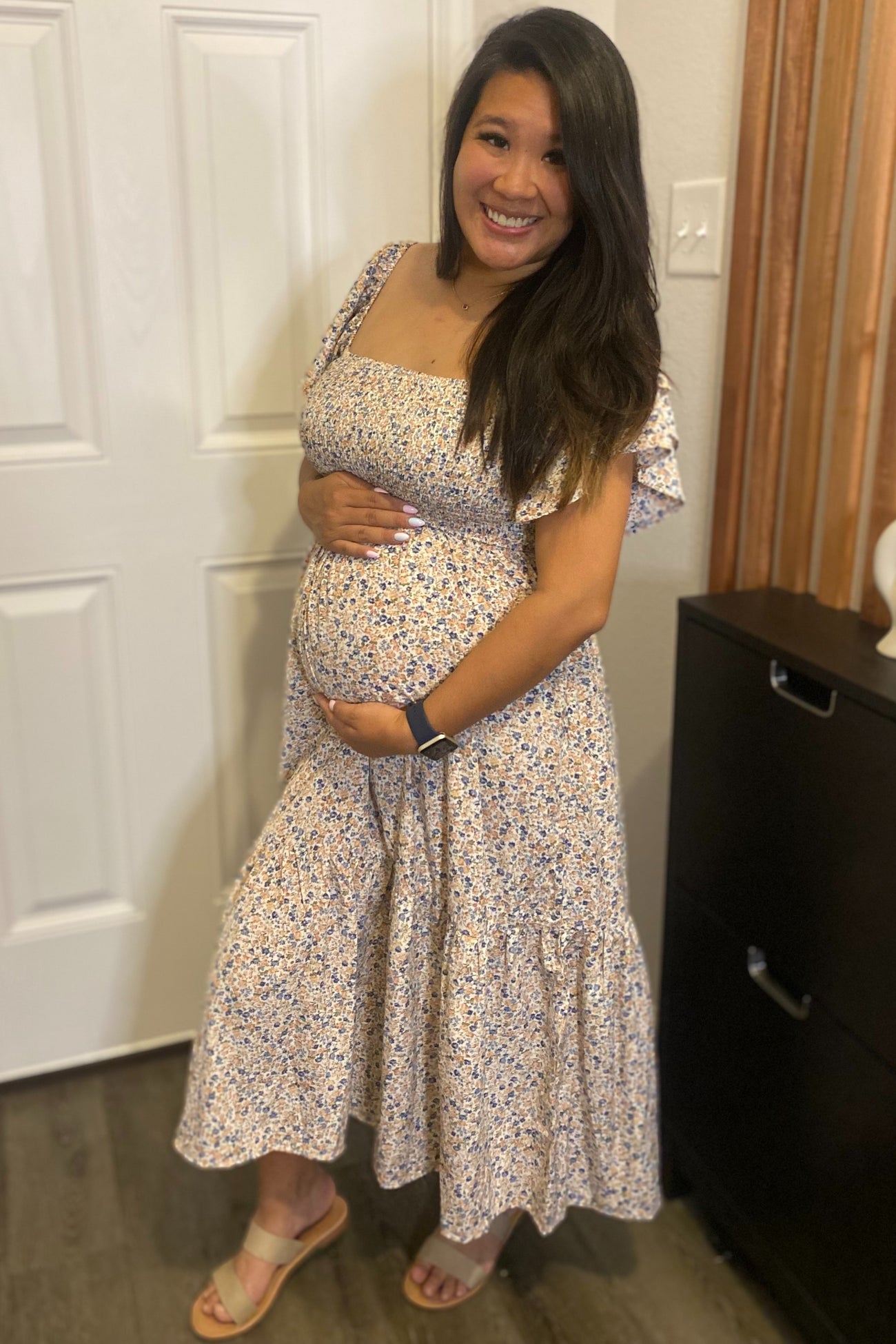 woman wearing a floral maternity dress with ruffled sleeves, smiling and holding her baby bump