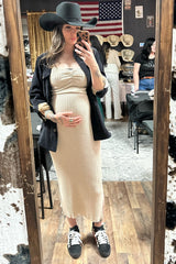 woman wearing a ribbed beige maternity dress with a black blazer and hat, holding her baby bump in a mirror selfie