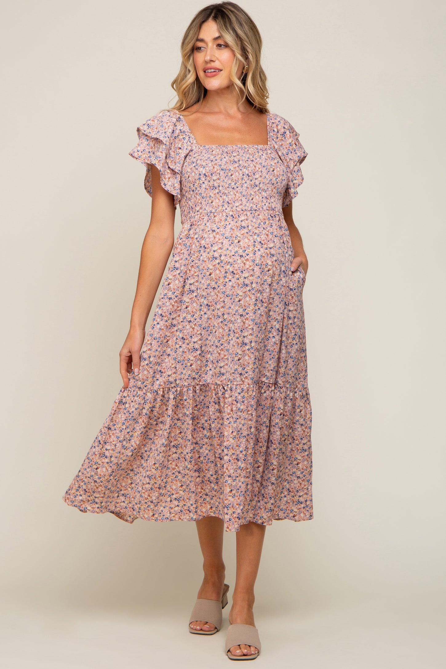 woman wearing a floral print maternity dress with ruffle sleeves and a flowing hem, showcasing her baby bump