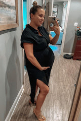 woman wearing a black maternity button-up dress with a side slit, gently cradling her baby bump