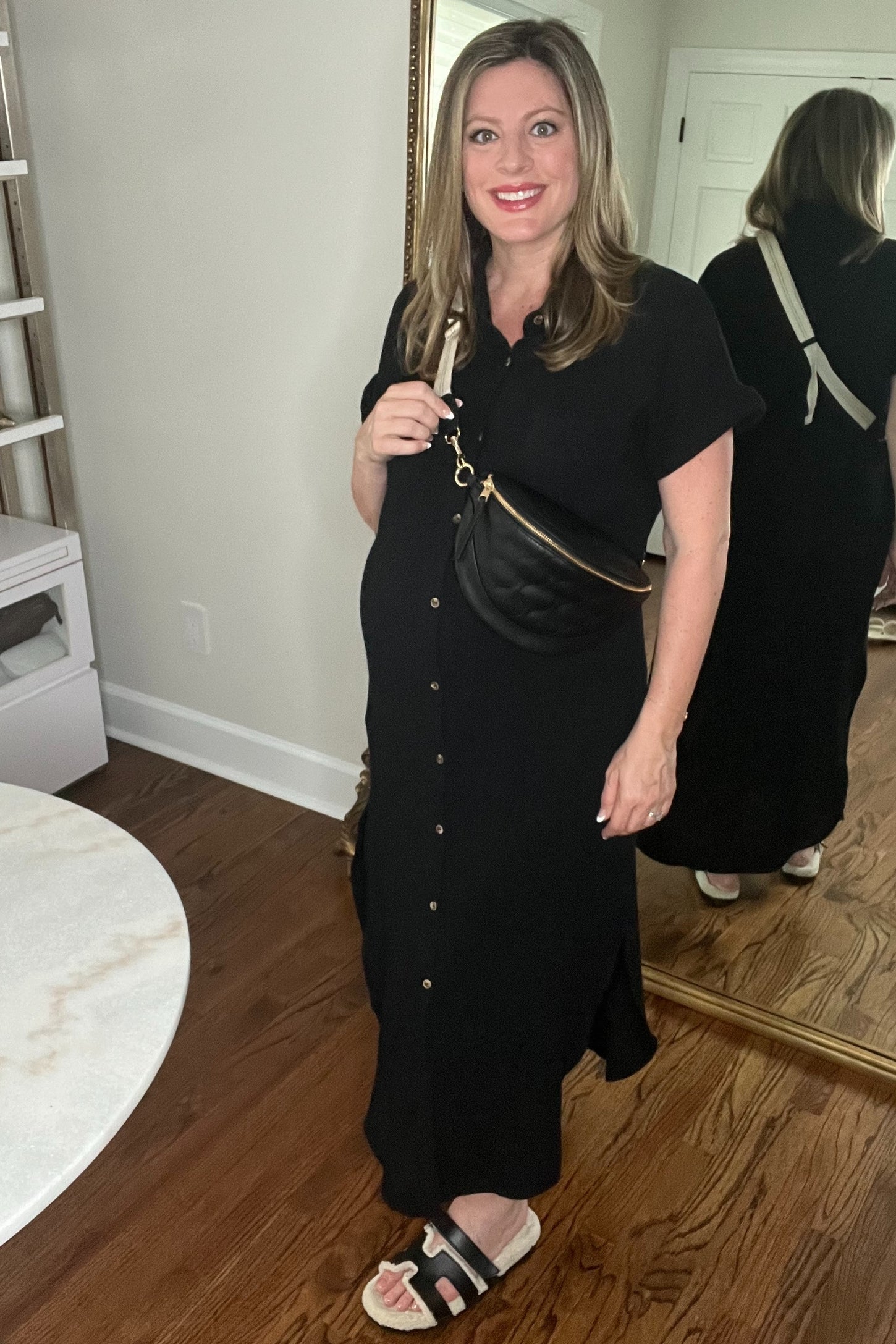 woman wearing a black maternity dress with buttons, holding a black crossbody bag, and showing a baby bump
