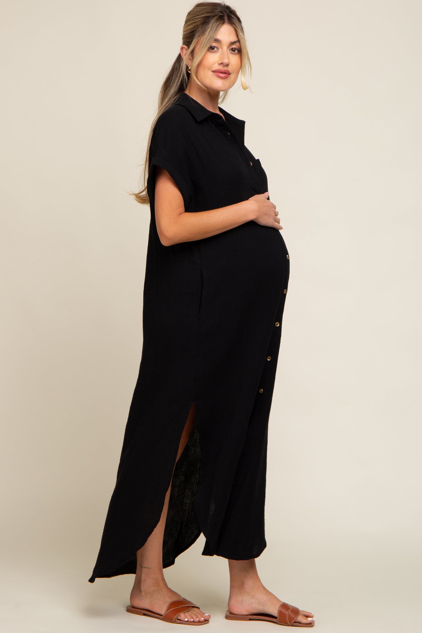 pregnant woman wearing a black short sleeve button down maternity maxi dress with side slits and brown sandals