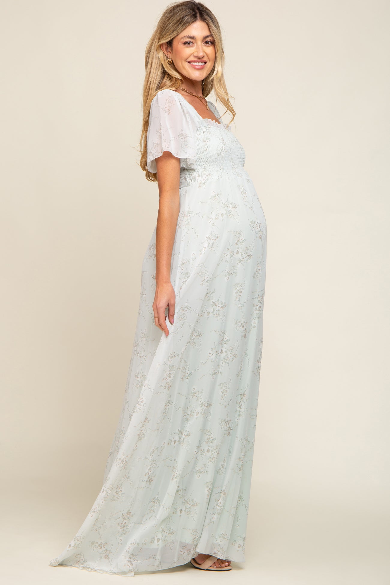 woman wearing a light green floral maternity dress with short puff sleeves and a visible baby bump