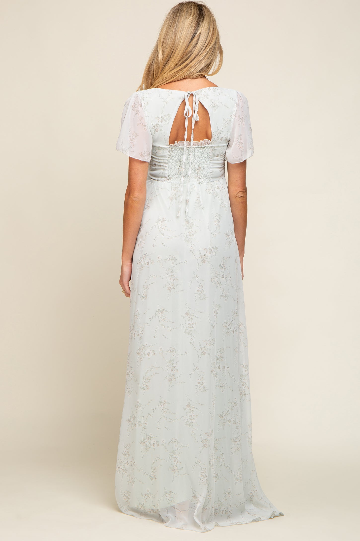 woman wearing a light blue maternity dress with sheer sleeves and a smocked back detail, showing a baby bump