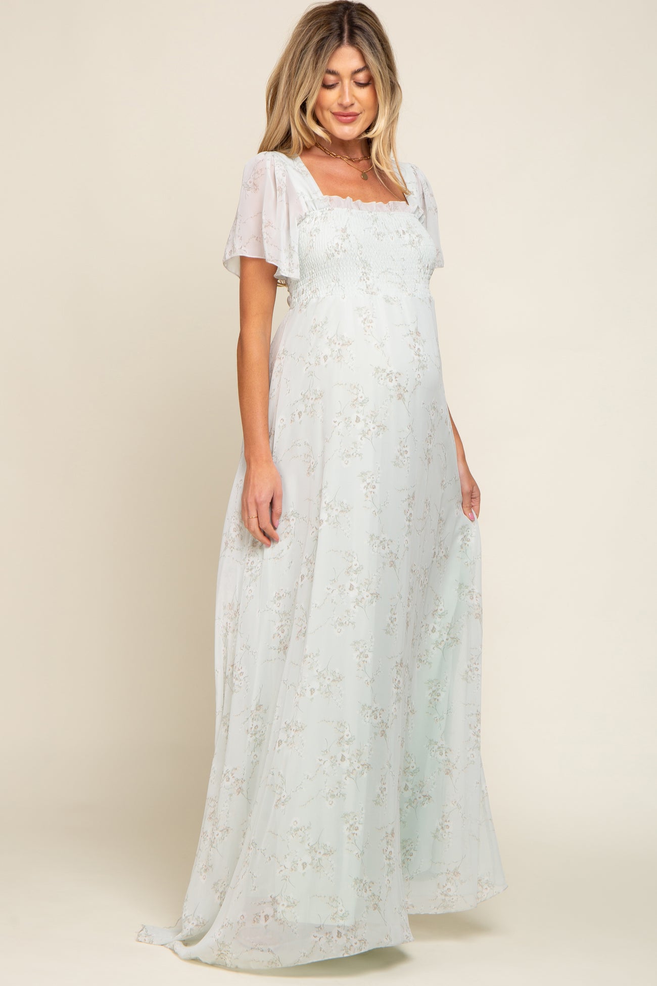 woman wearing a light green floral maternity maxi dress with puff sleeves and a smocked bodice, showing her baby bump