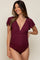 woman wearing a burgundy maternity swimsuit with a deep v-neck and ruffled sleeves, showcasing her baby bump