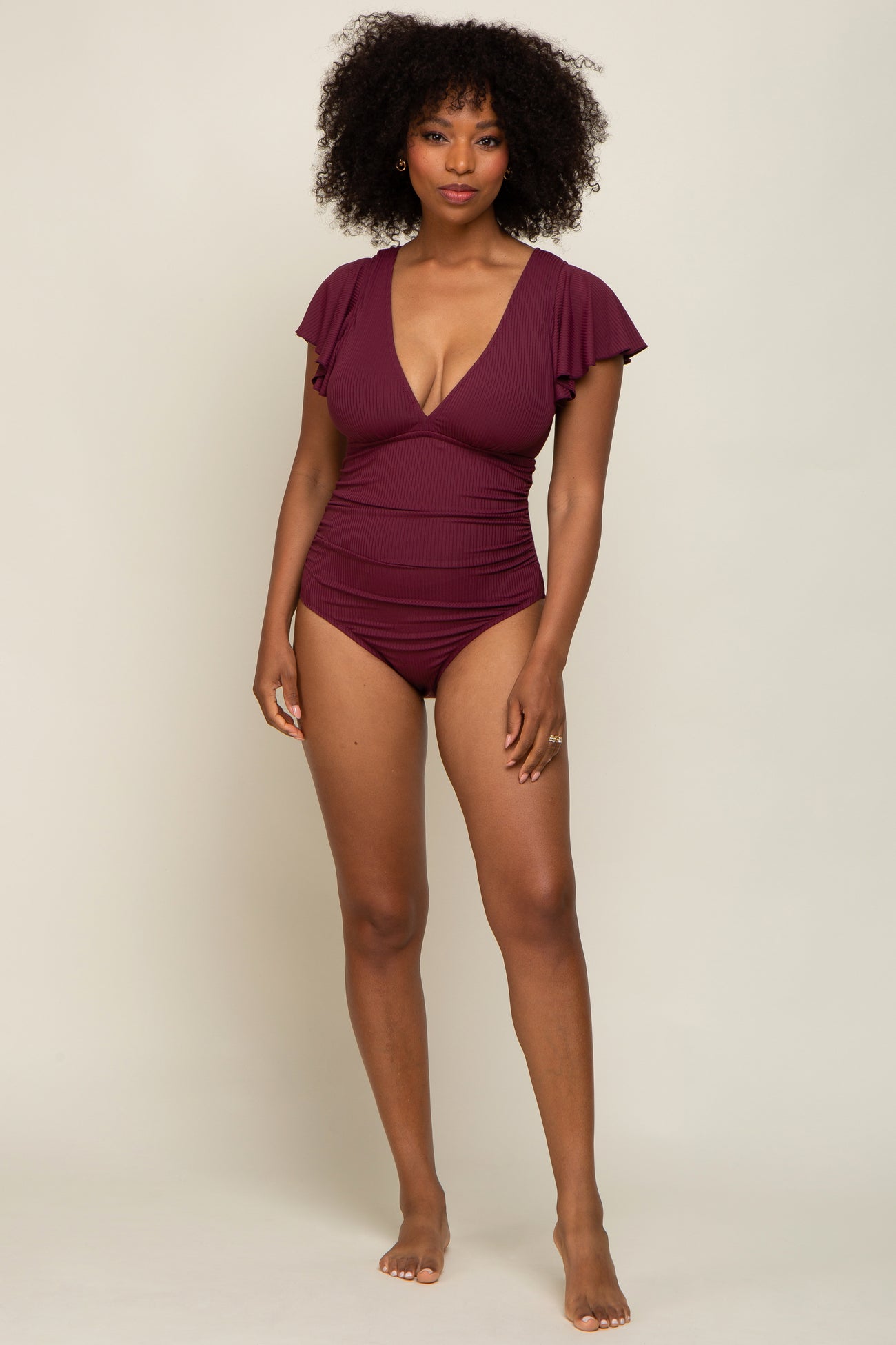woman wearing a burgundy one-piece swimsuit with ruffle sleeves and a plunging neckline