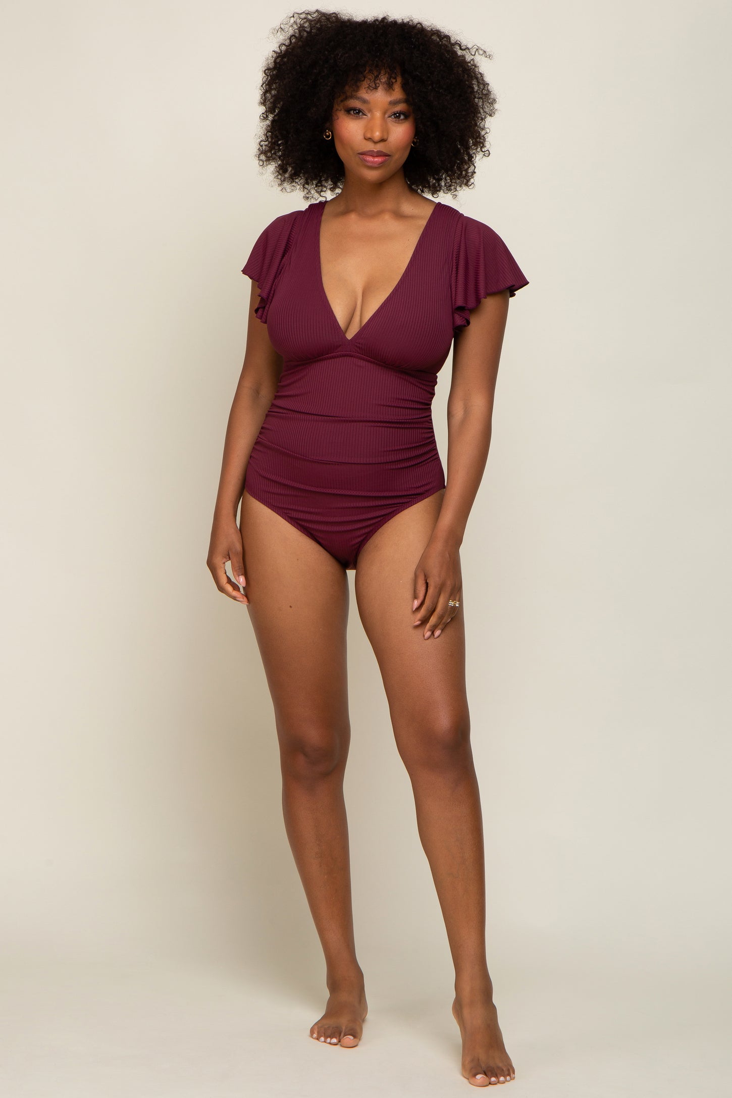 woman wearing a burgundy one-piece swimsuit with ruffle sleeves and a plunging neckline