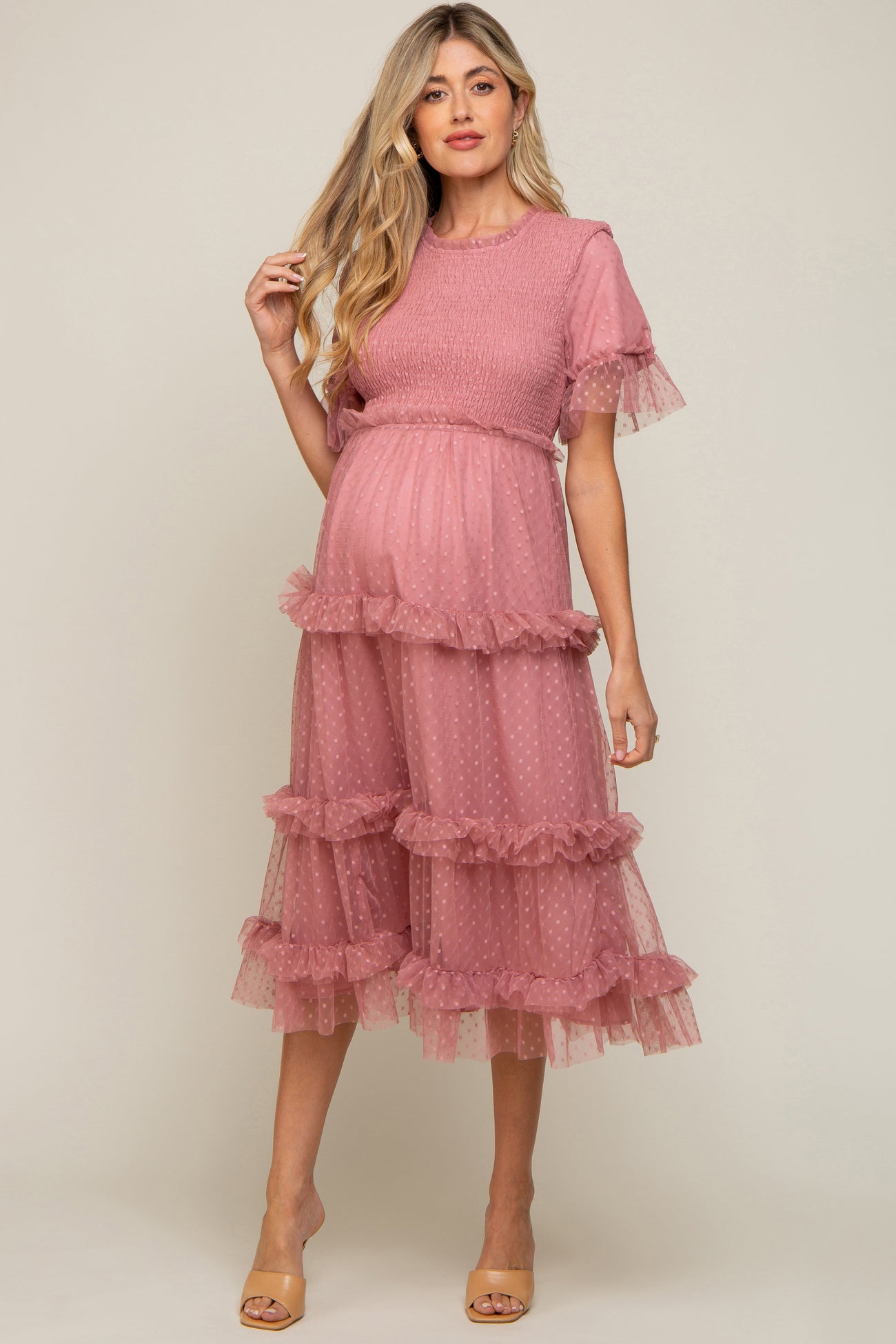 woman wearing a blush pink maternity dress with ruffled layers and short sleeves, showcasing her baby bump