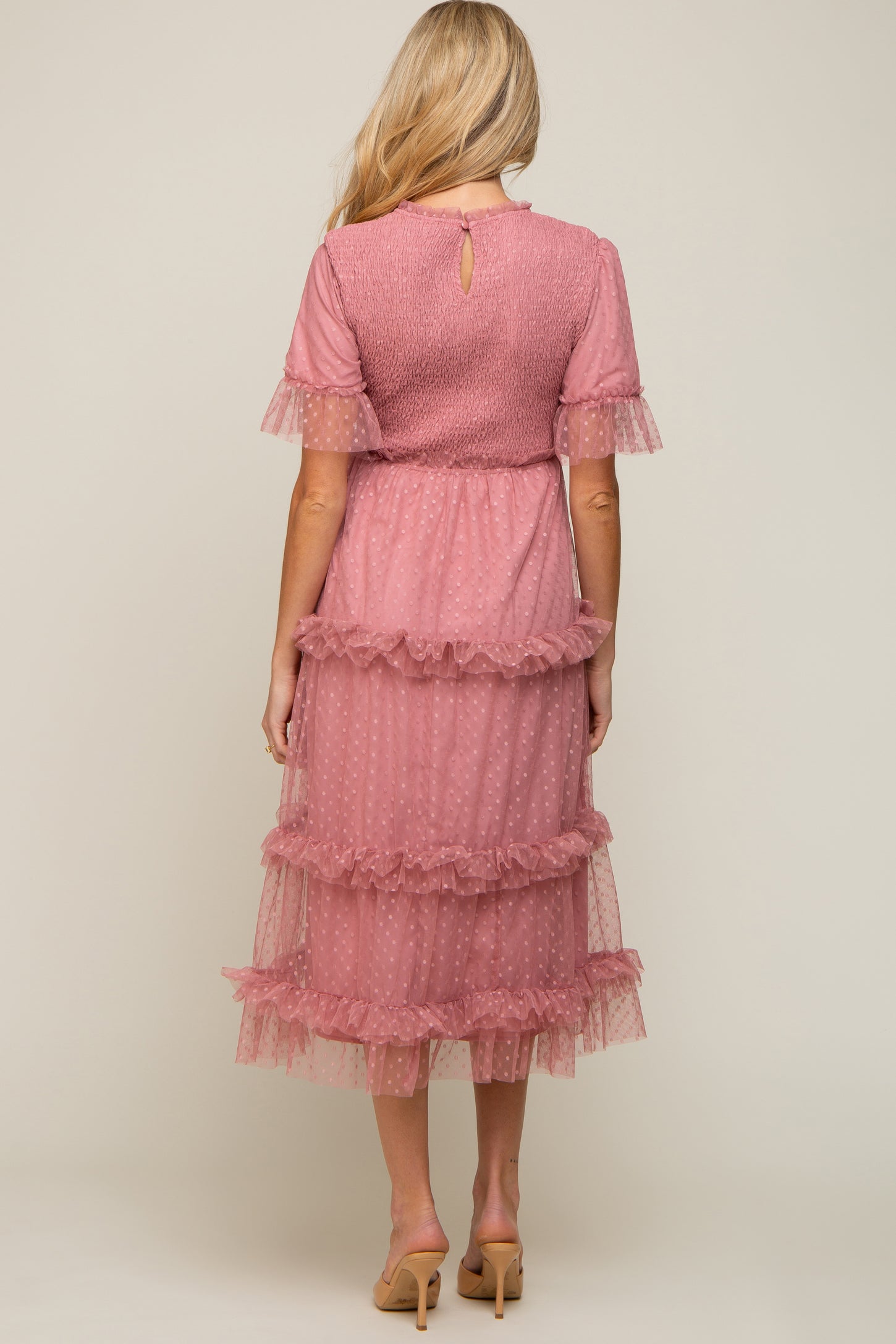 woman wearing a pink polka dot maternity dress with ruffled layers and short sleeves, viewed from the back