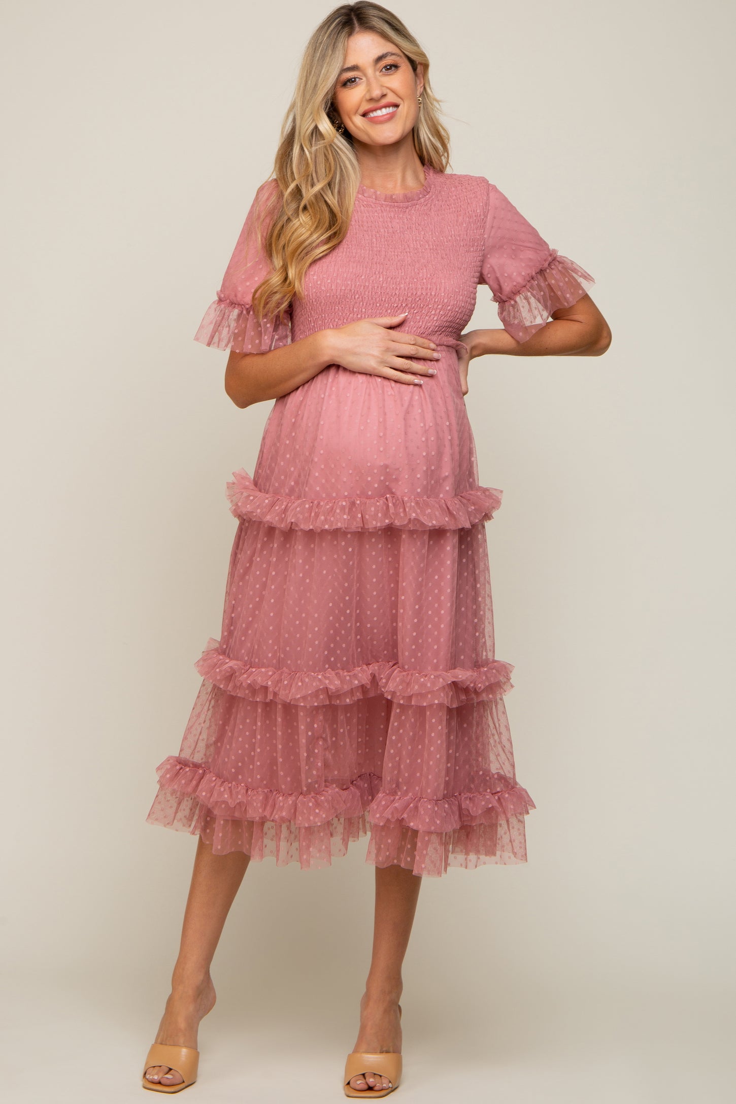 woman wearing a pink maternity dress with ruffle details and a tiered design, holding her baby bump