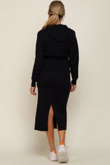 woman wearing a black maternity hoodie dress with a back slit, styled with white sneakers