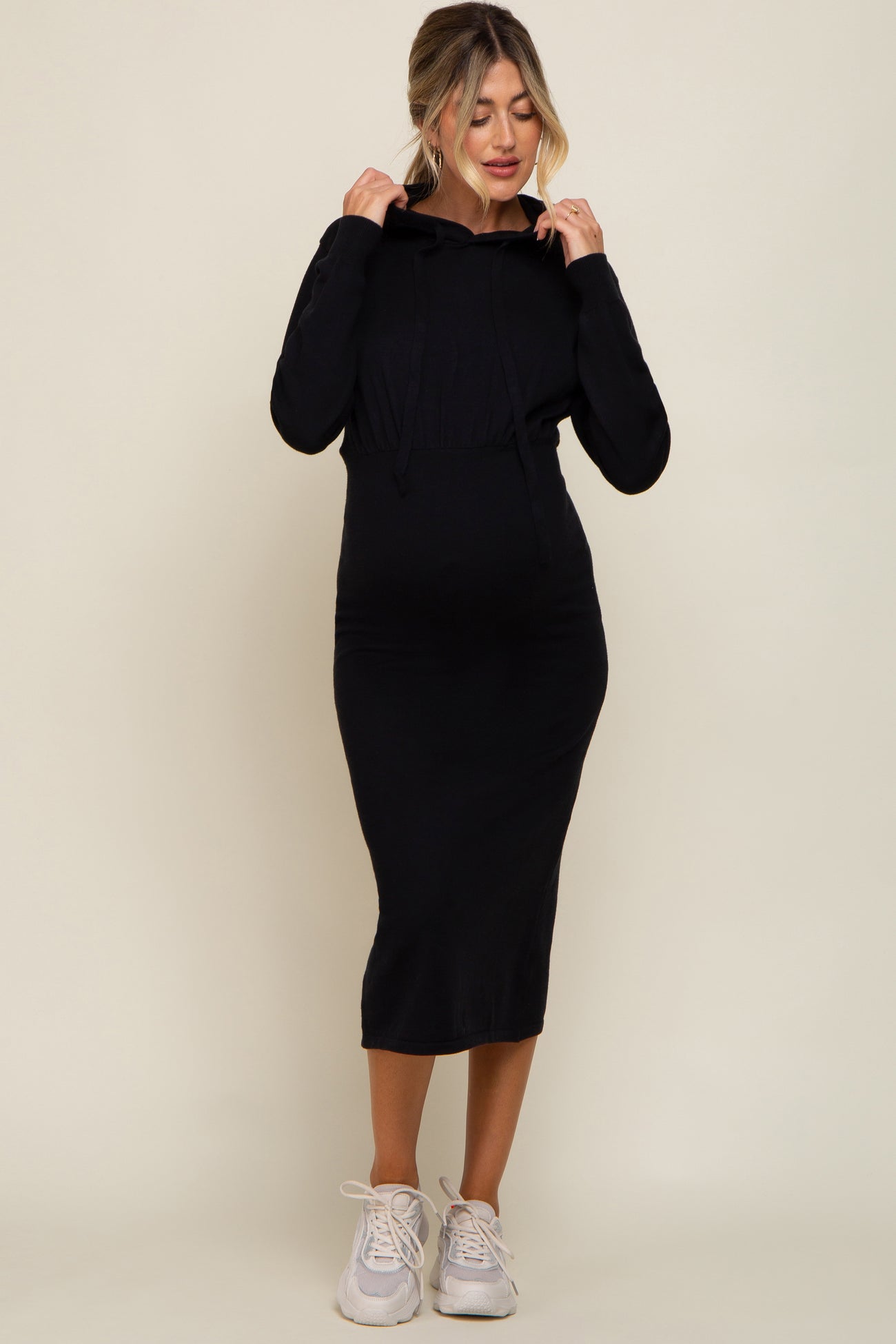 woman wearing a black maternity hoodie dress with a fitted silhouette and sneakers, showcasing her baby bump