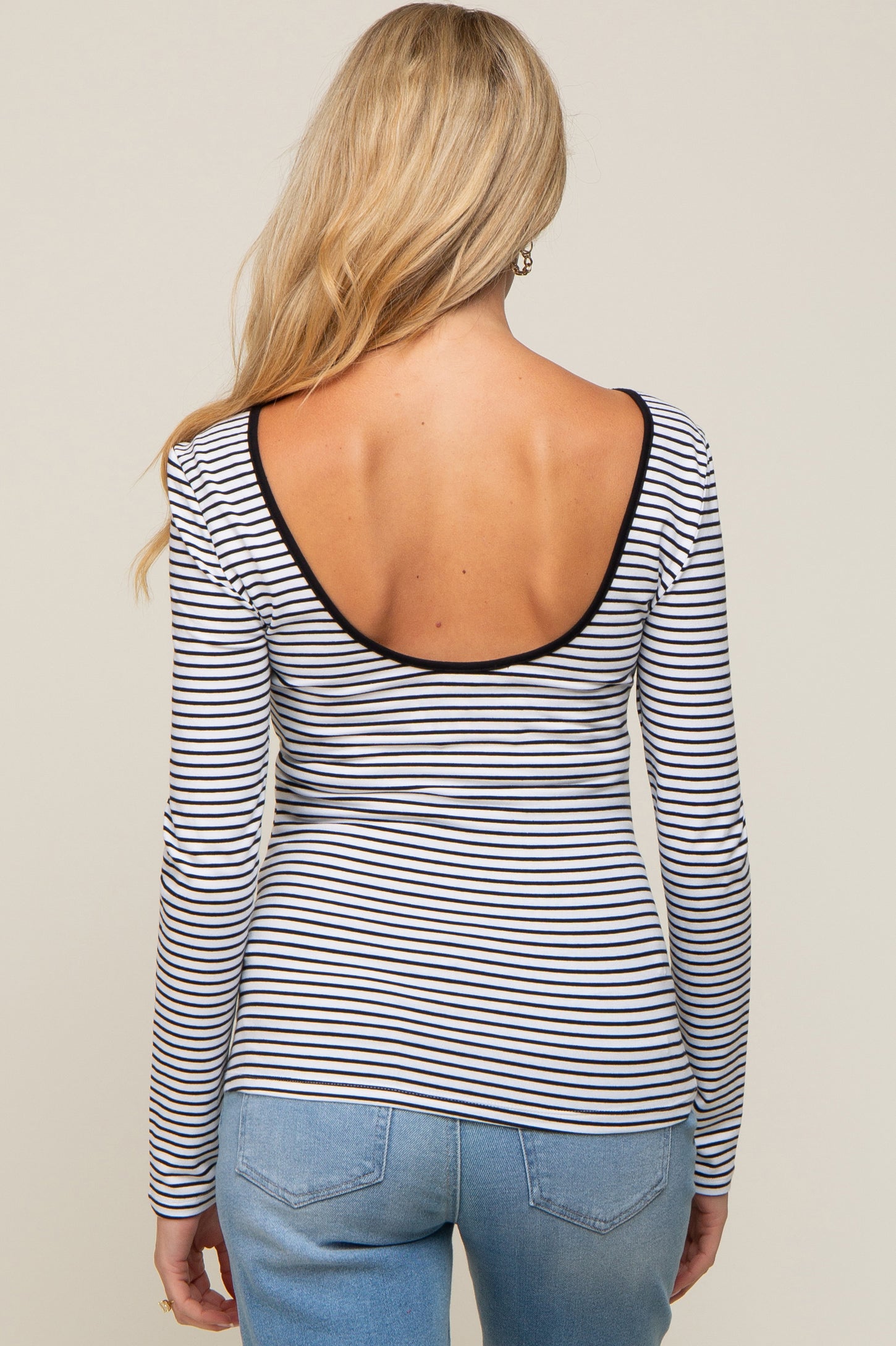 woman wearing a striped maternity top with a low back and long sleeves, paired with light blue jeans