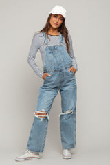woman wearing a striped long sleeve maternity top with distressed denim overalls and a white cap, hands in pockets