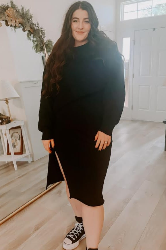 woman wearing a black long sleeve dress with a side slit and styled with black sneakers