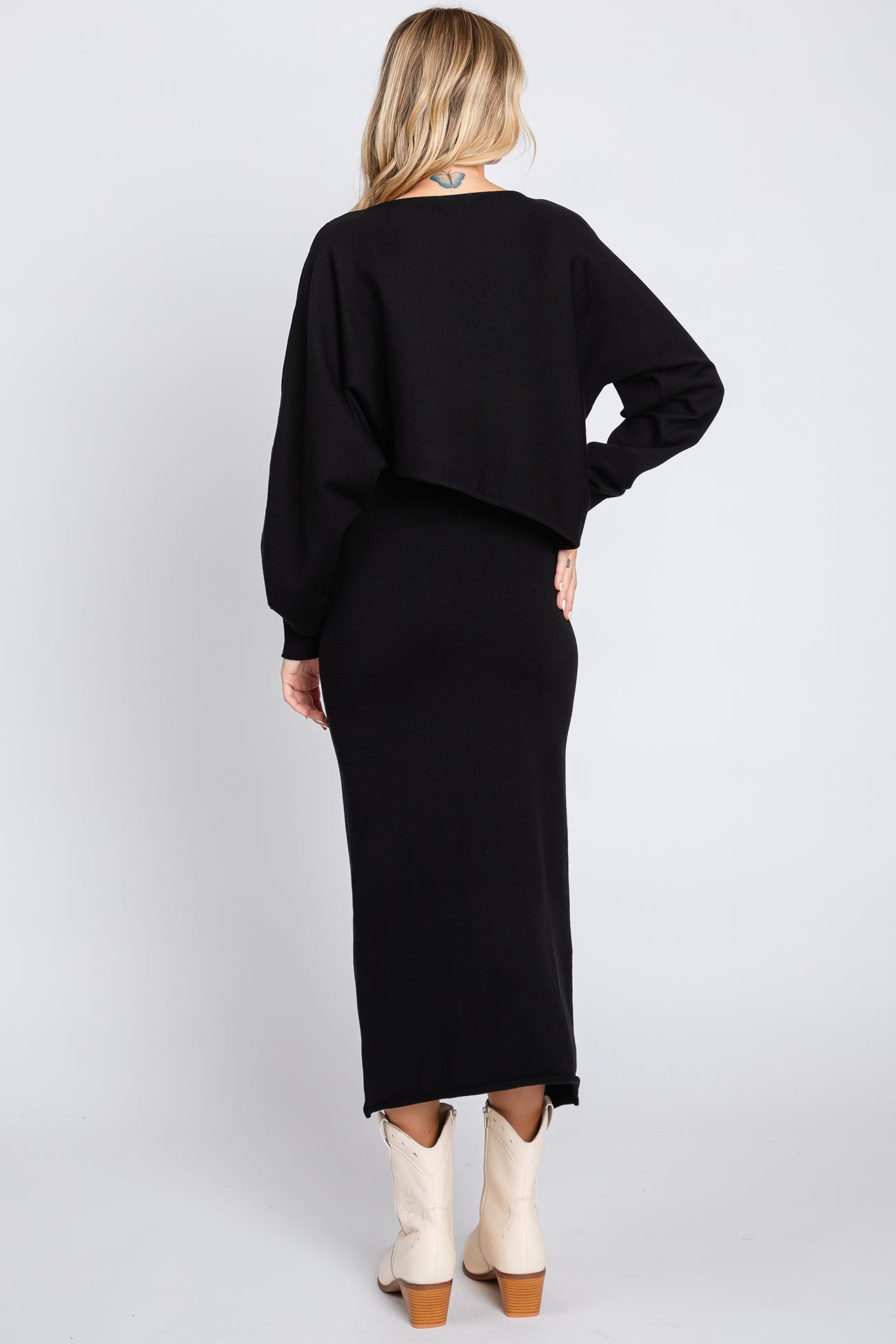 woman wearing a black long sleeve cropped sweater over a black fitted maxi dress and cream ankle boots