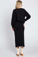 woman wearing a black long sleeve cropped sweater over a black fitted maxi dress and cream ankle boots