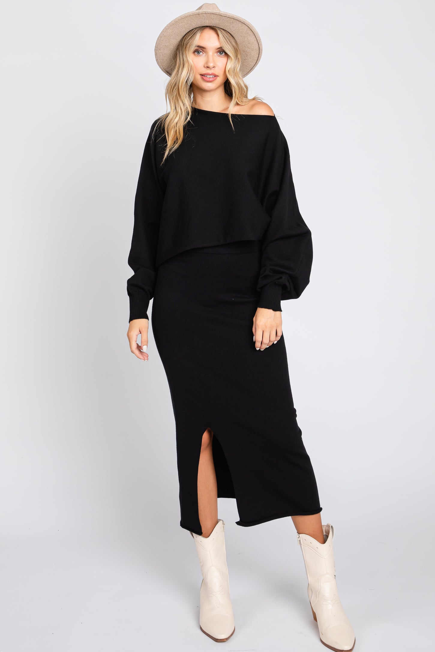 woman wearing a black off-the-shoulder cropped sweater and a black midi skirt with a side slit, paired with white cowboy boots