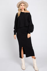 woman wearing a black off-the-shoulder cropped sweater and a black midi skirt with a side slit, paired with white cowboy boots