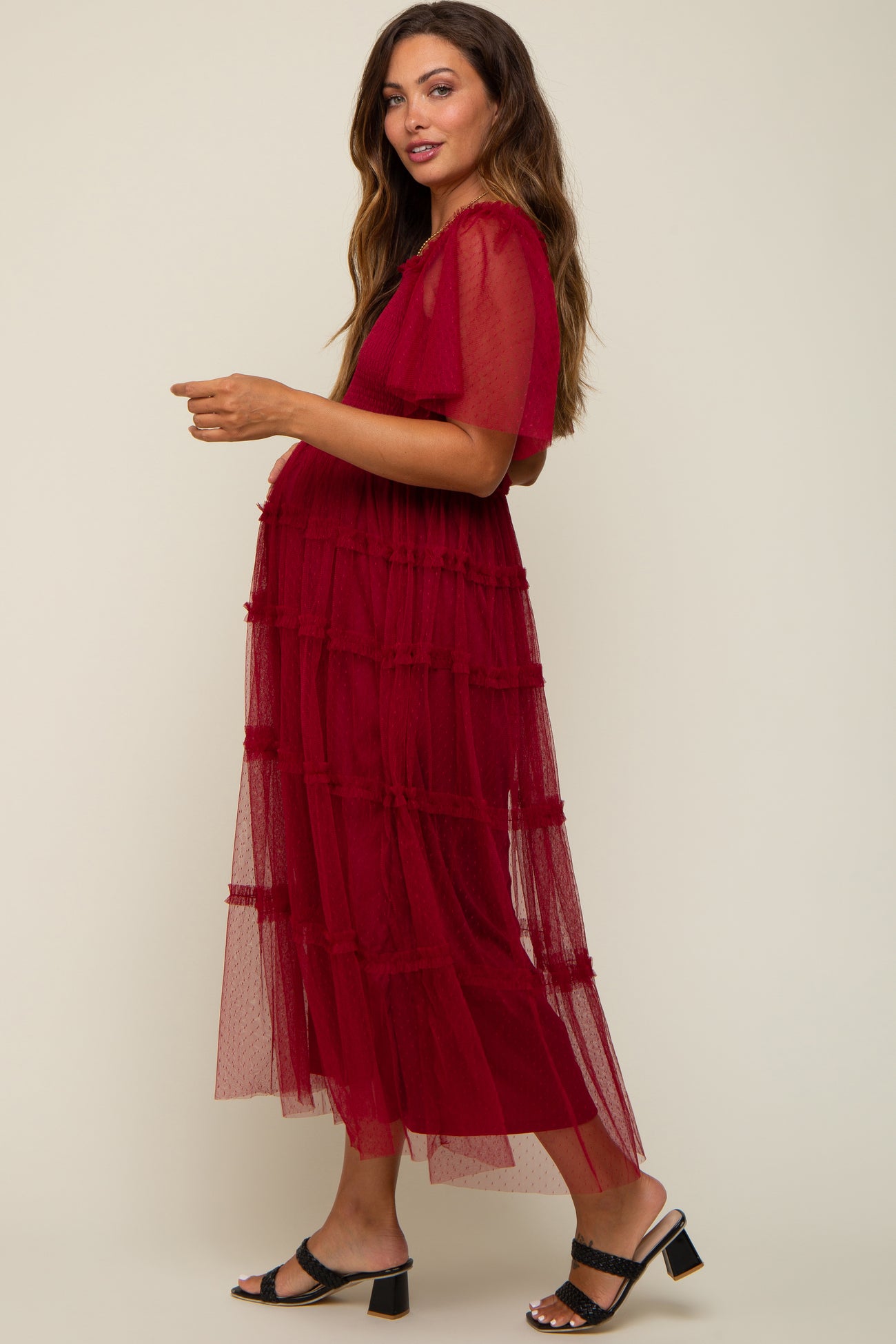 woman wearing a red tiered tulle maternity dress with short sleeves and a visible baby bump