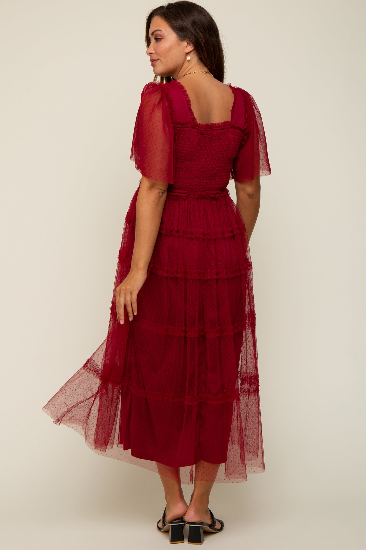 woman wearing a burgundy tiered maternity dress with sheer puff sleeves, showing a flowing silhouette from the back