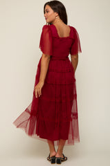woman wearing a burgundy tiered maternity dress with sheer puff sleeves, showing a flowing silhouette from the back