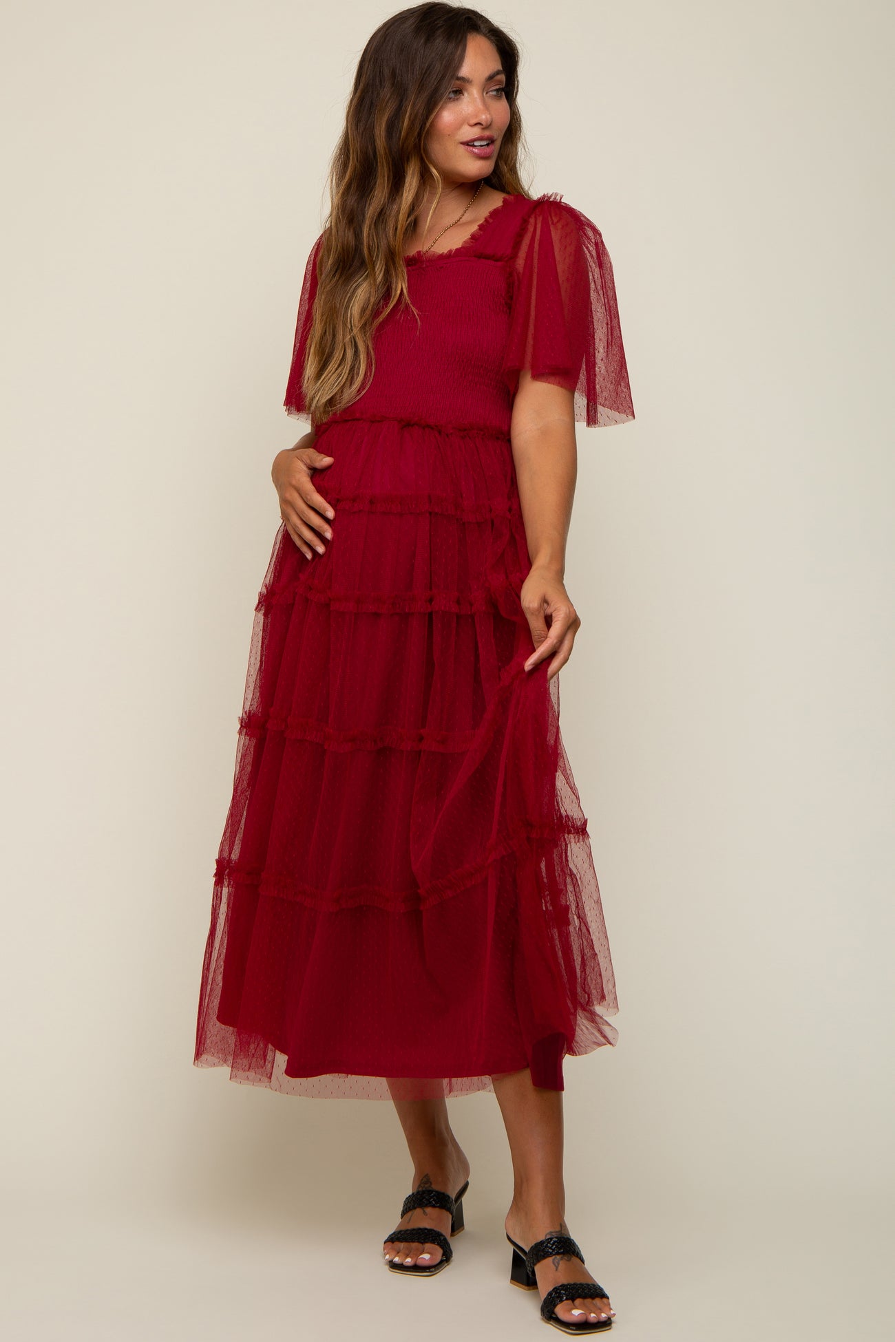 woman wearing a red maternity dress with sheer ruffled sleeves and a tiered design, showing her baby bump