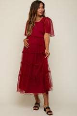 woman wearing a red maternity dress with sheer ruffled sleeves and a tiered design, showing her baby bump