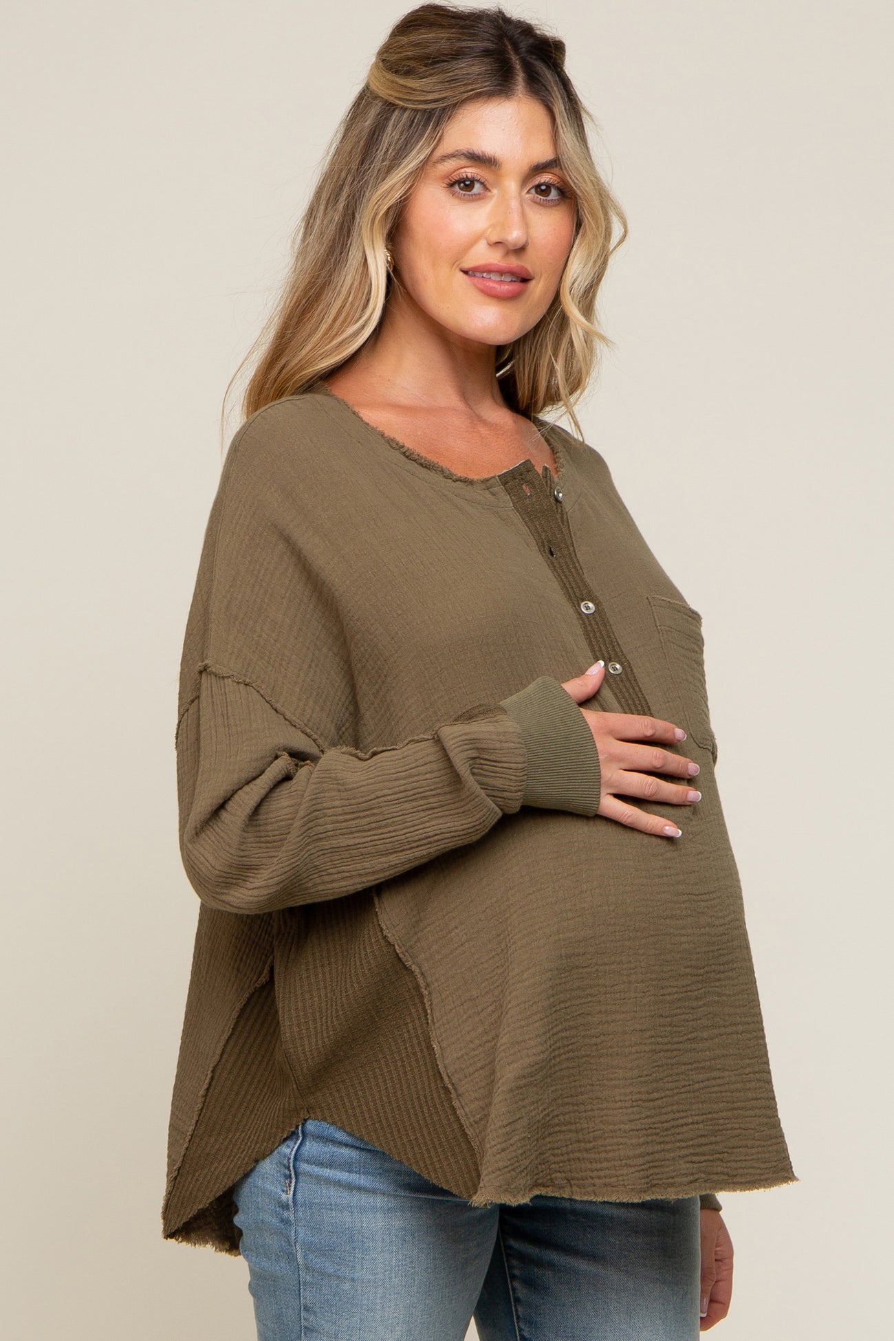 woman wearing an olive green maternity top with a henley neckline and a visible baby bump while smiling