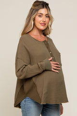 woman wearing an olive green maternity top with a henley neckline and a visible baby bump while smiling