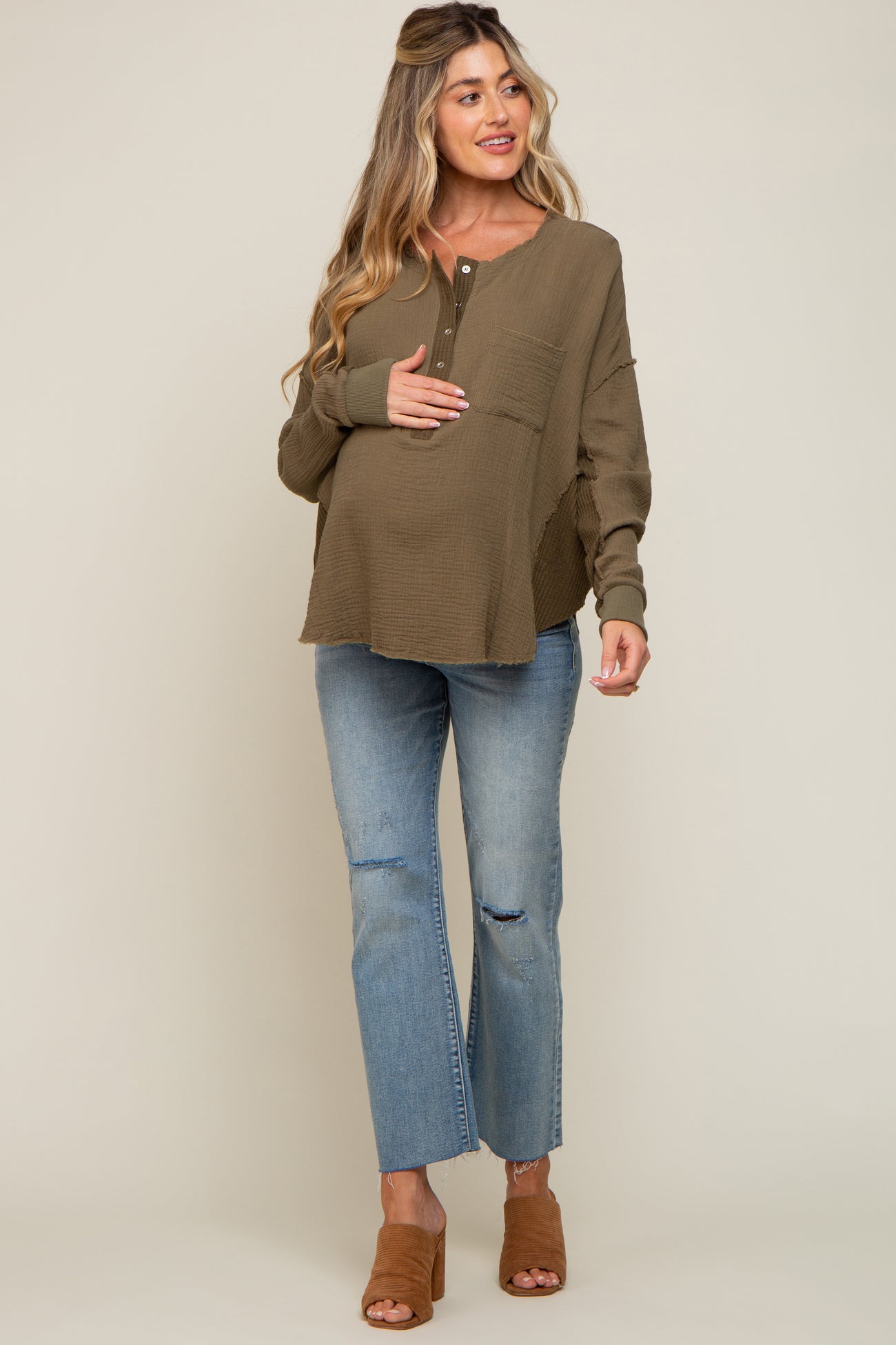 woman wearing a brown maternity top with a pocket and distressed light blue jeans, holding her baby bump