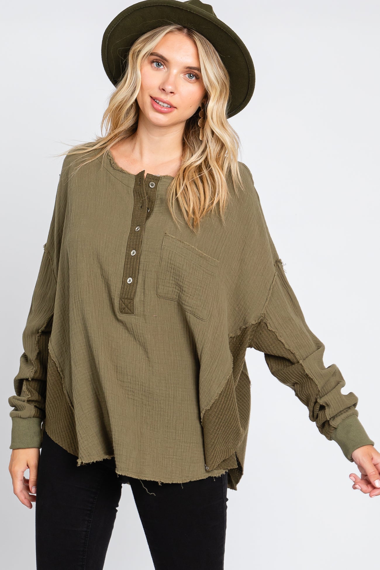 woman wearing an olive green long sleeve oversized henley top with a pocket and distressed detailing, paired with a hat