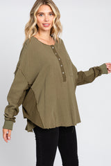 woman wearing an oversized olive green long sleeve button-up top with a pocket and raw hem, paired with black pants