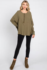 woman wearing an olive green long sleeve oversized top with buttons and black skinny jeans, styled with brown ankle boots