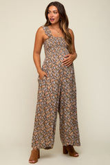woman wearing a brown floral maternity jumpsuit with pockets, showing her baby bump