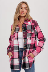 woman wearing a pink and black plaid flannel shirt jacket over a white tank top with front pockets and button closure