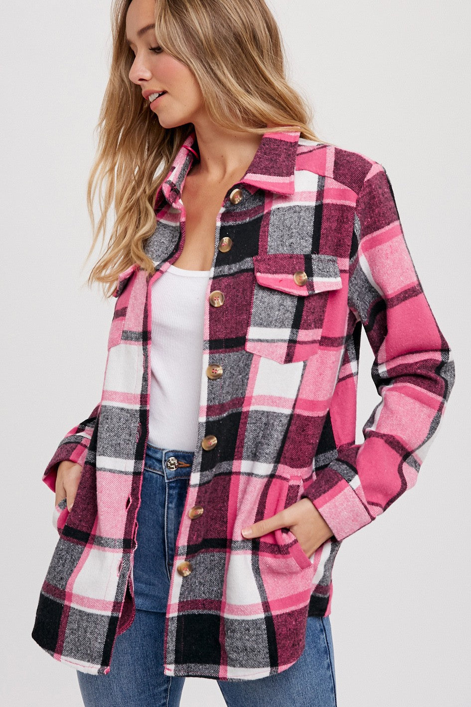 woman wearing a pink and black plaid shacket with chest pockets and button closure styled with a white tank top and jeans
